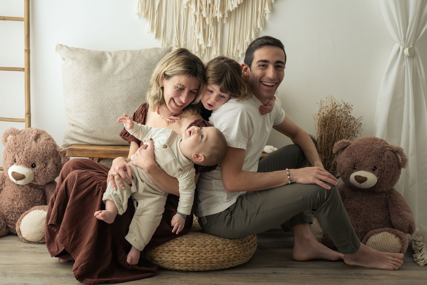 Una famiglia di 4 persone gioca e si diverte durante un servizio fotografico in uno studio dai toni naturali, dove ci sono due orsetti.