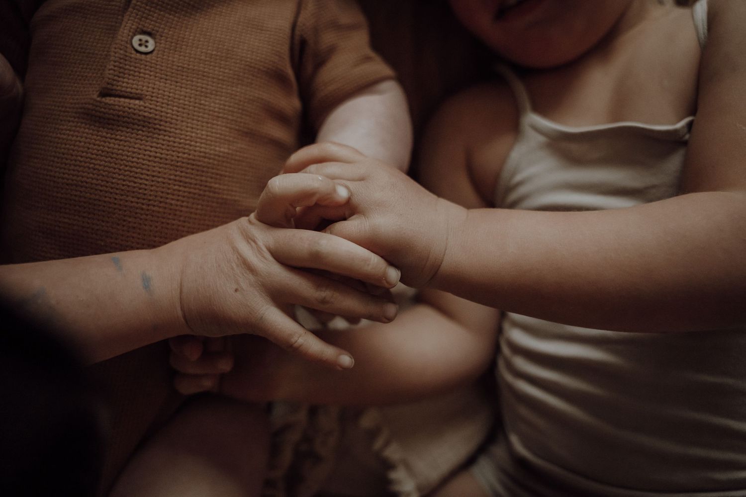 handjes van kinderen bij elkaar, een baby op de achtergrond. Geen gezichten zichtbaar.