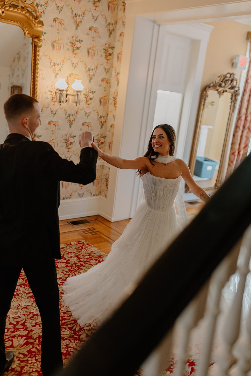 Dancing couple in formal attire twirling in elegant room with floral wallpaper.