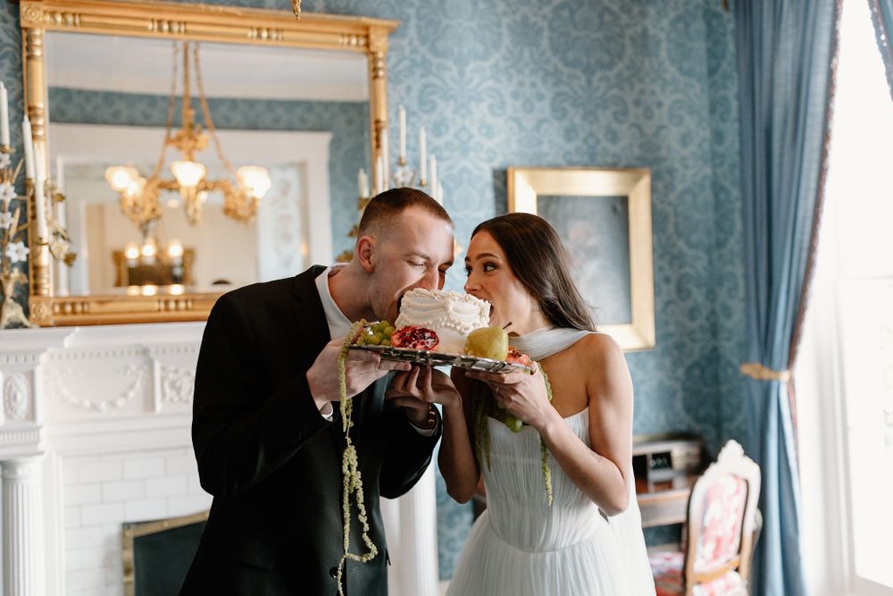 Couple sharing champagne toast in elegant blue room with ornate fireplace.