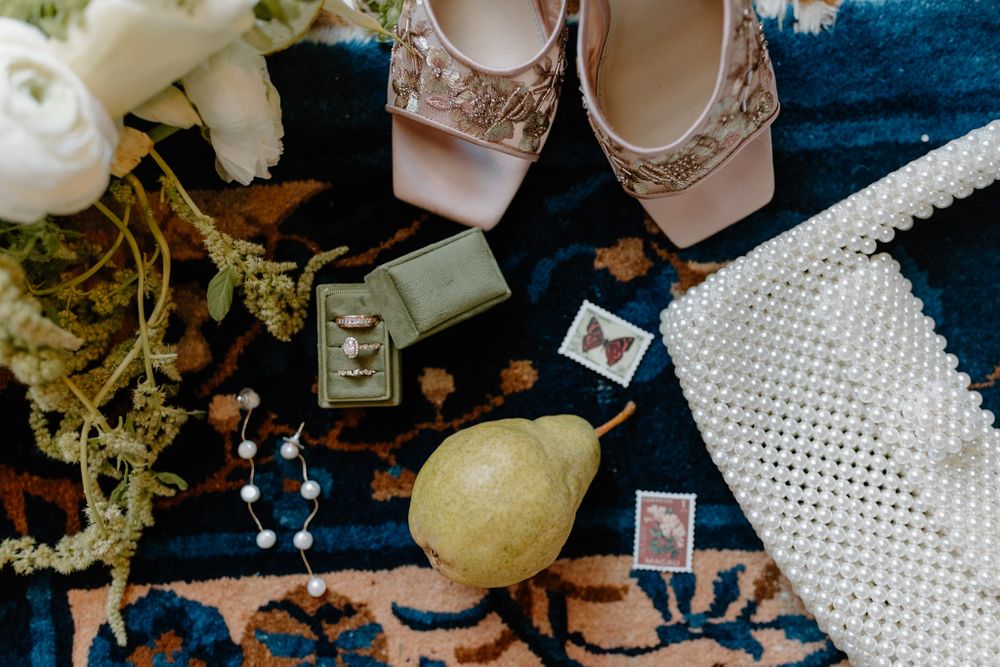 Wedding accessories including pink shoes, jewelry and flowers arranged on blue patterned rug.