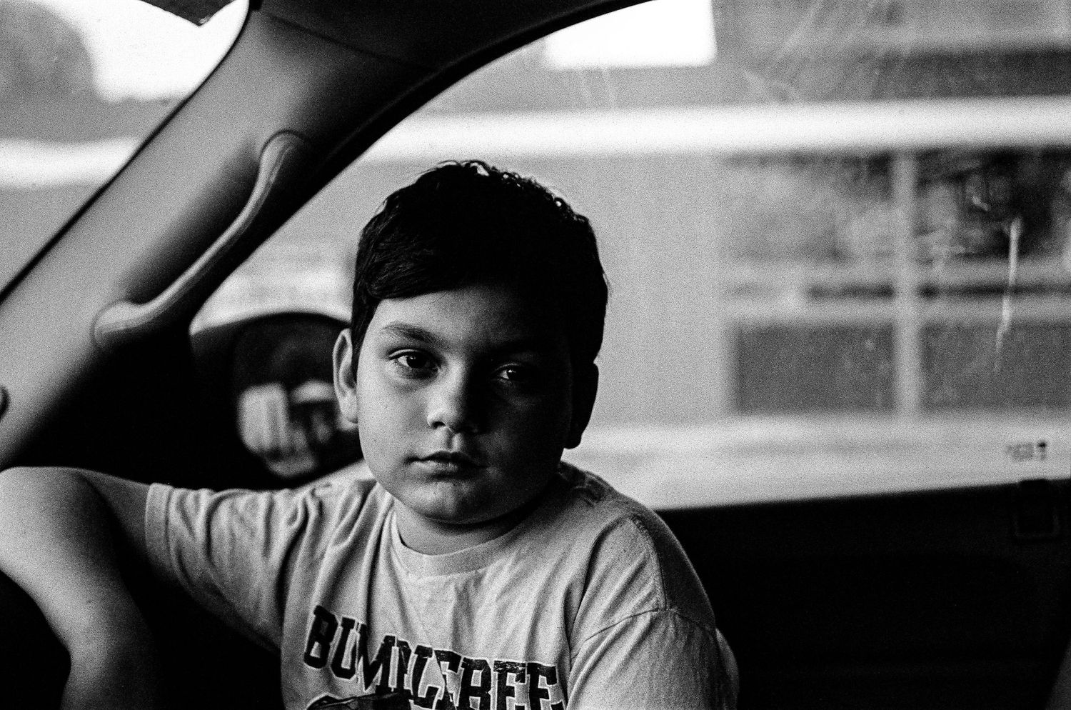 Black and white photograph of a child in Los Angeles t-shirt sitting in a car.