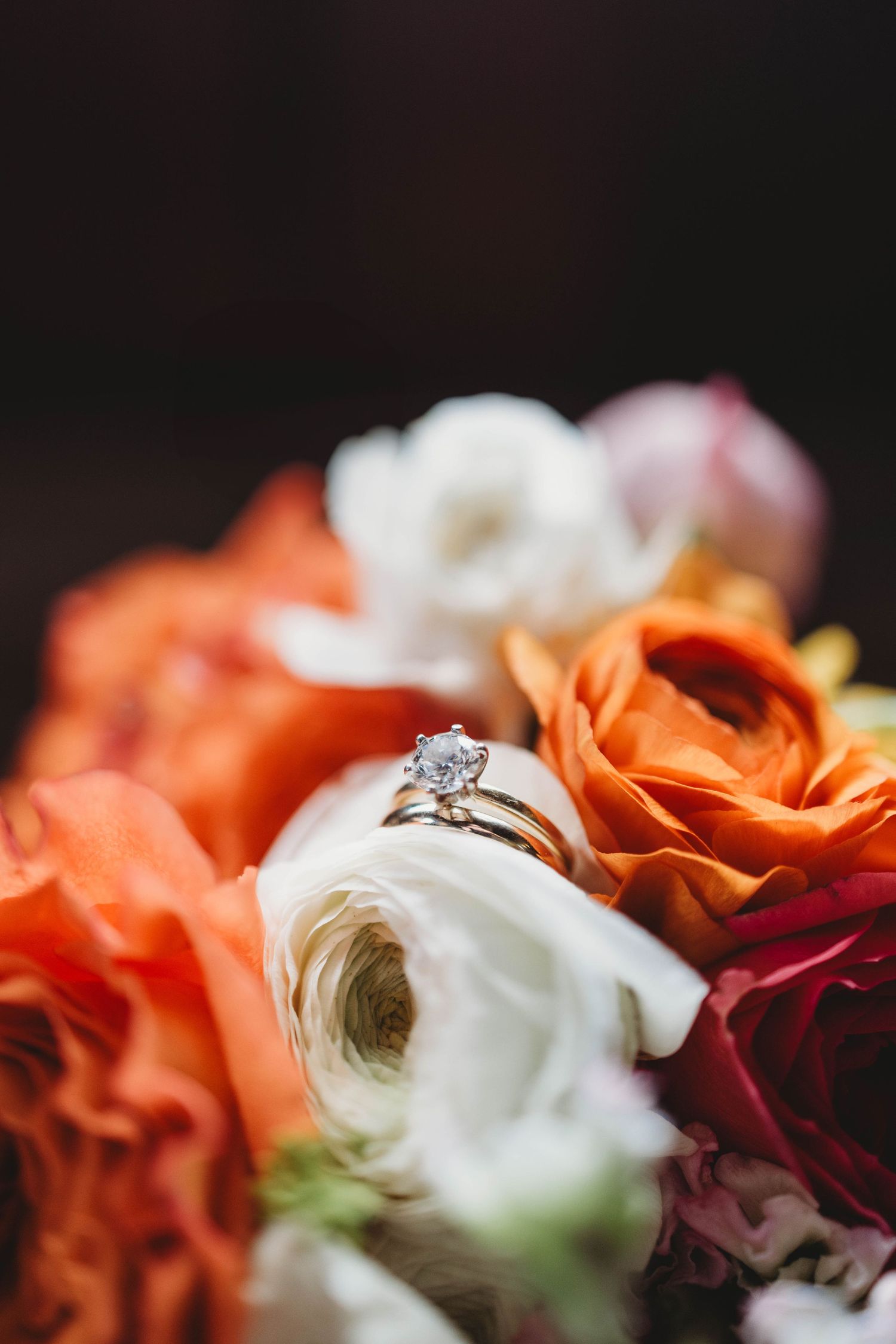 Diamond engagement ring nestled among orange and white roses in a romantic close-up shot.