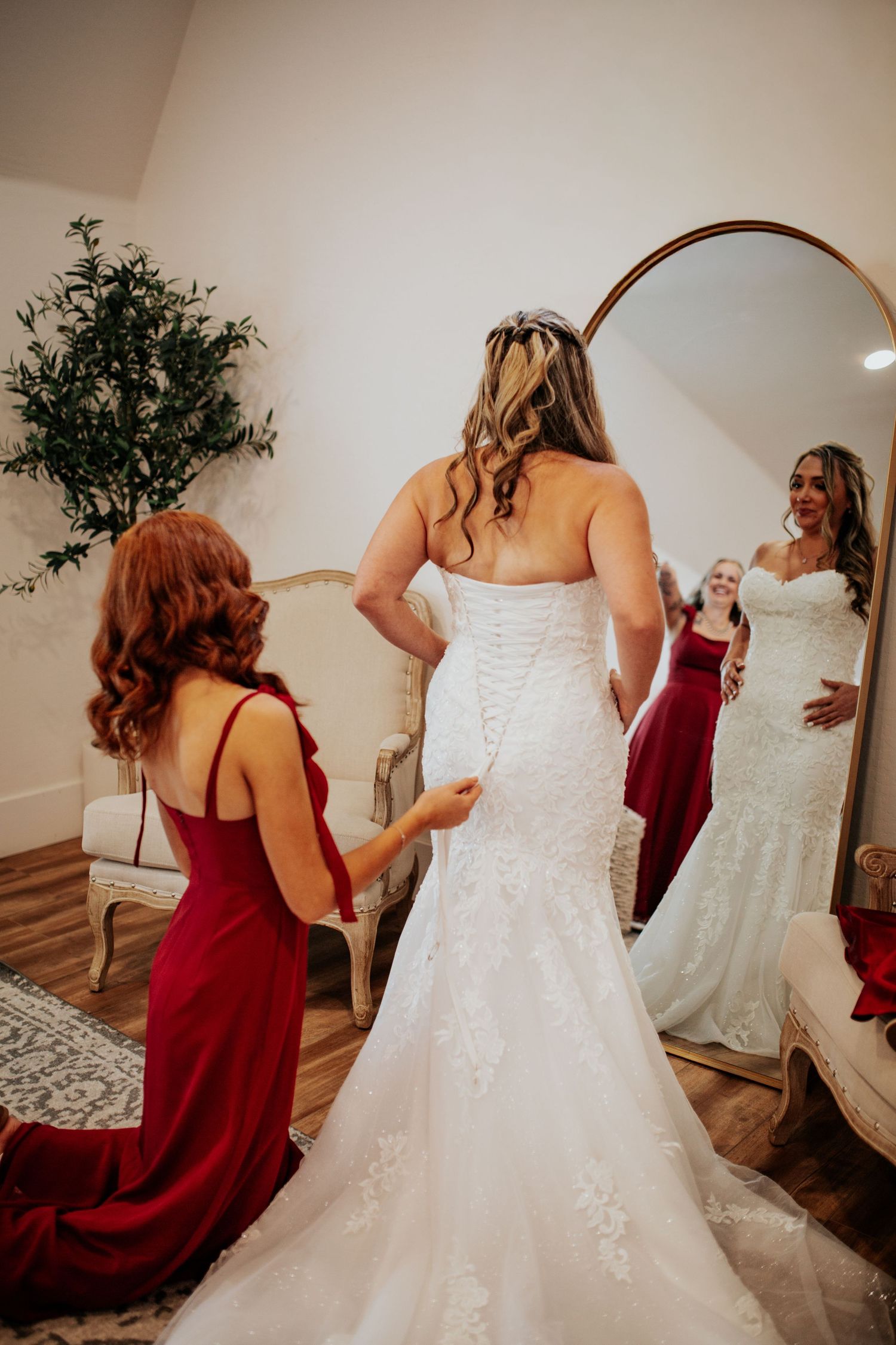 Wedding preparation scene with bridesmaids in burgundy dresses helping with a white bridal gown.