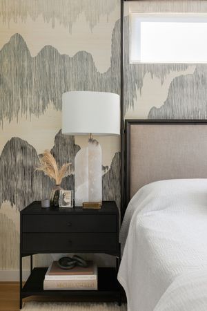Modern bedroom nightstand with lamp and abstract wallpaper design.