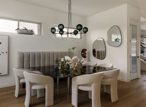 Modern dining area with grey upholstered bench seating, white chairs, and black spherical chandelier fixture.