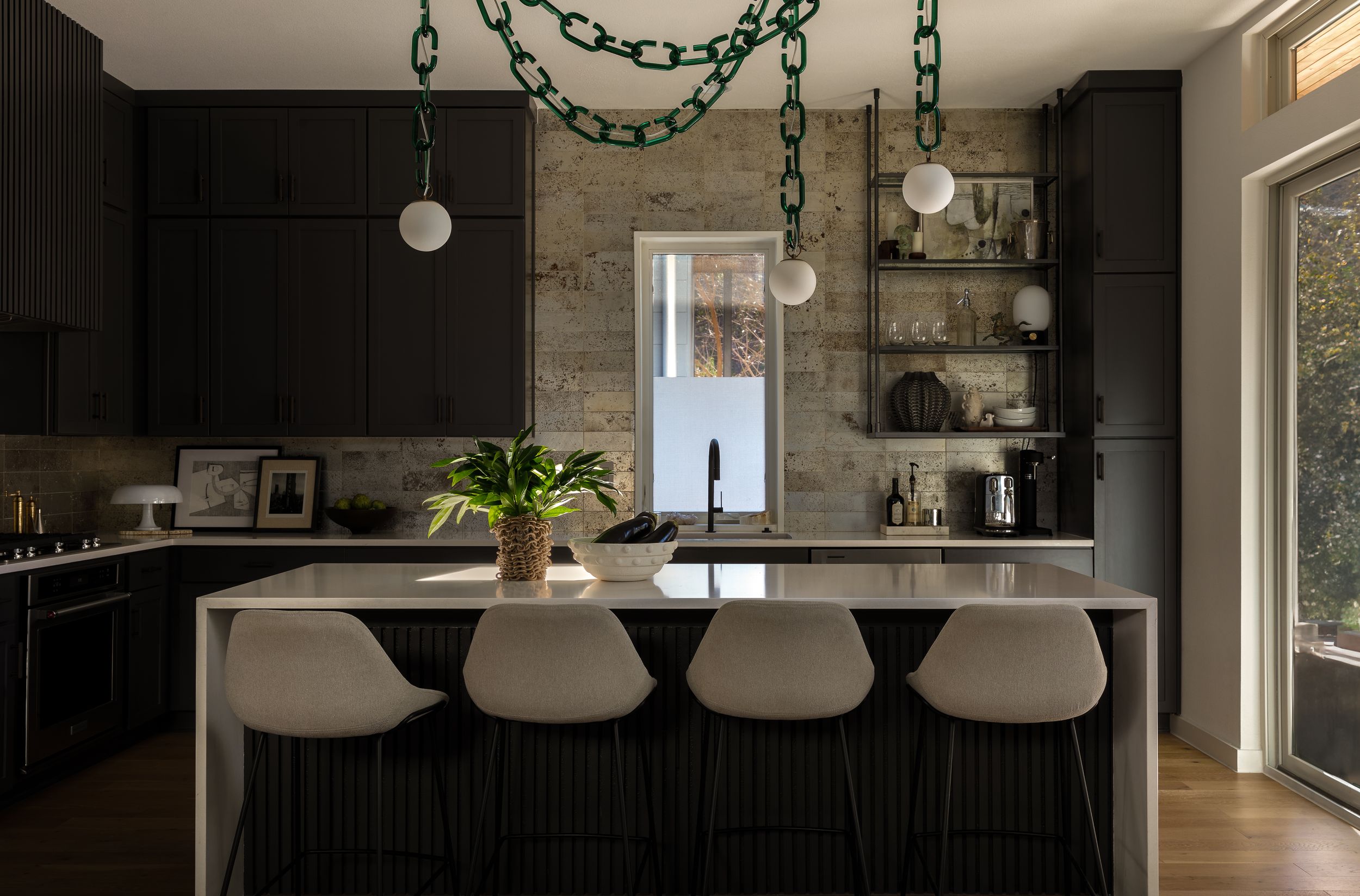 Contemporary black kitchen with white bar stools and unique green chain pendant lights.