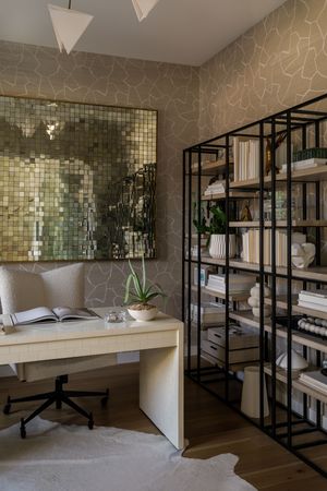 Modern home office with metallic tile wall art, black shelving unit, and minimalist white desk setup.