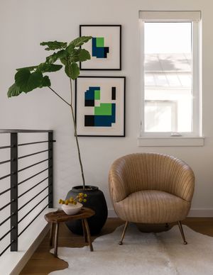 Stylish corner nook with geometric wall art, large fiddle leaf fig plant, and ribbed tan accent chair.