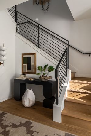 Modern staircase with black metal railings and wooden steps leading upstairs, featuring a sleek console table.