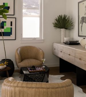Elegant sitting area with tan curved chairs, geometric art prints, and a modern white credenza.
