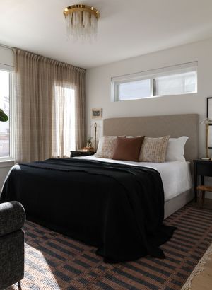 Contemporary bedroom with taupe headboard, black bedding, and sheer curtains under clerestory windows.