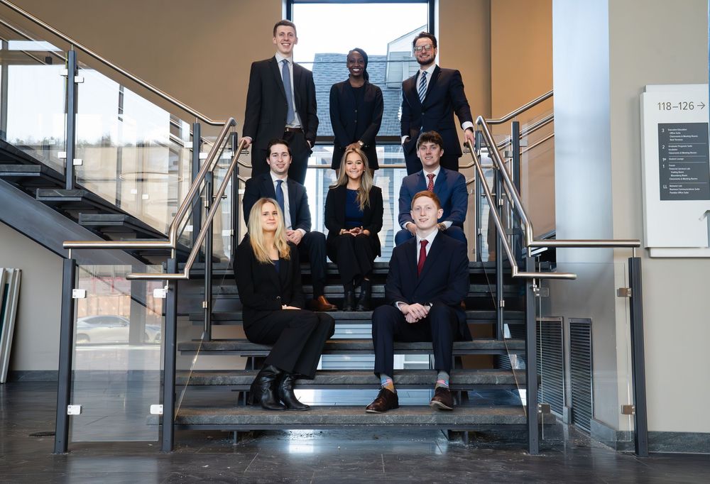 A professional group of nine business people posing on modern office stairs in formal attire.