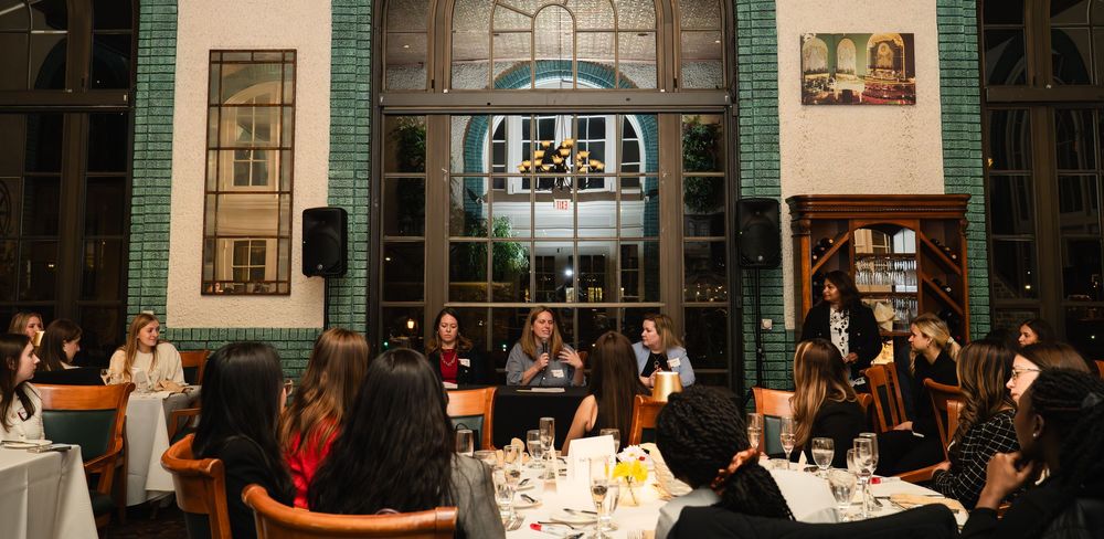 A panoramic view of a business meeting room with people seated around tables during a professional conference or presentation.