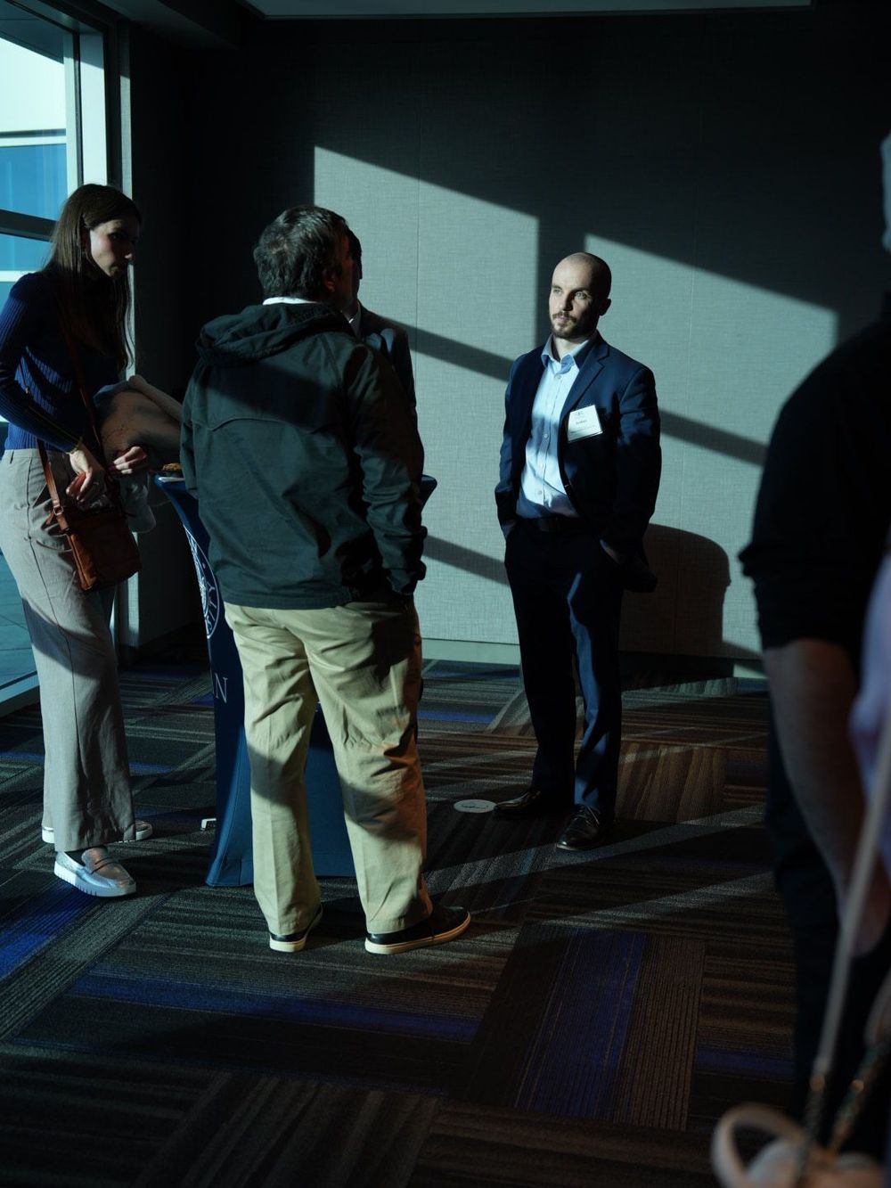 Business professionals networking in a modern conference venue with dramatic natural lighting through large windows.