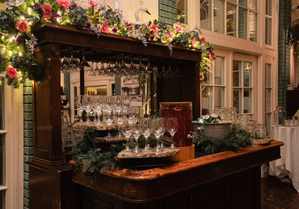 Elegant wooden bar adorned with floral garlands, hanging wine glasses, and greenery at an upscale event venue.