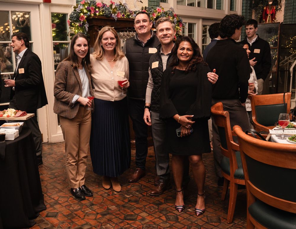 Group of five professionals smiling together at an elegant indoor networking event with festive holiday decor.