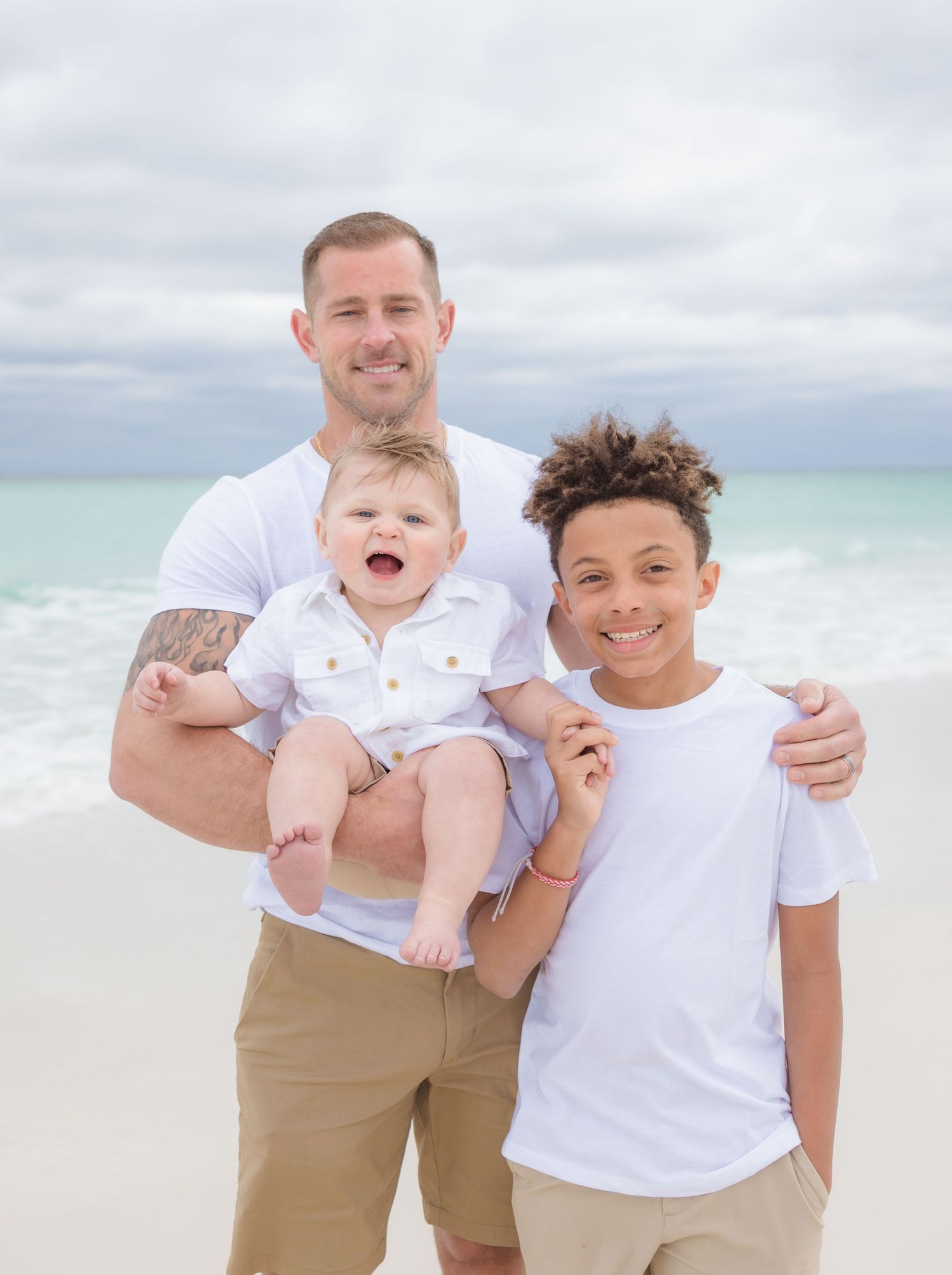 A joyful family portrait on a beautiful beach with turquoise water and cloudy skies in the background.