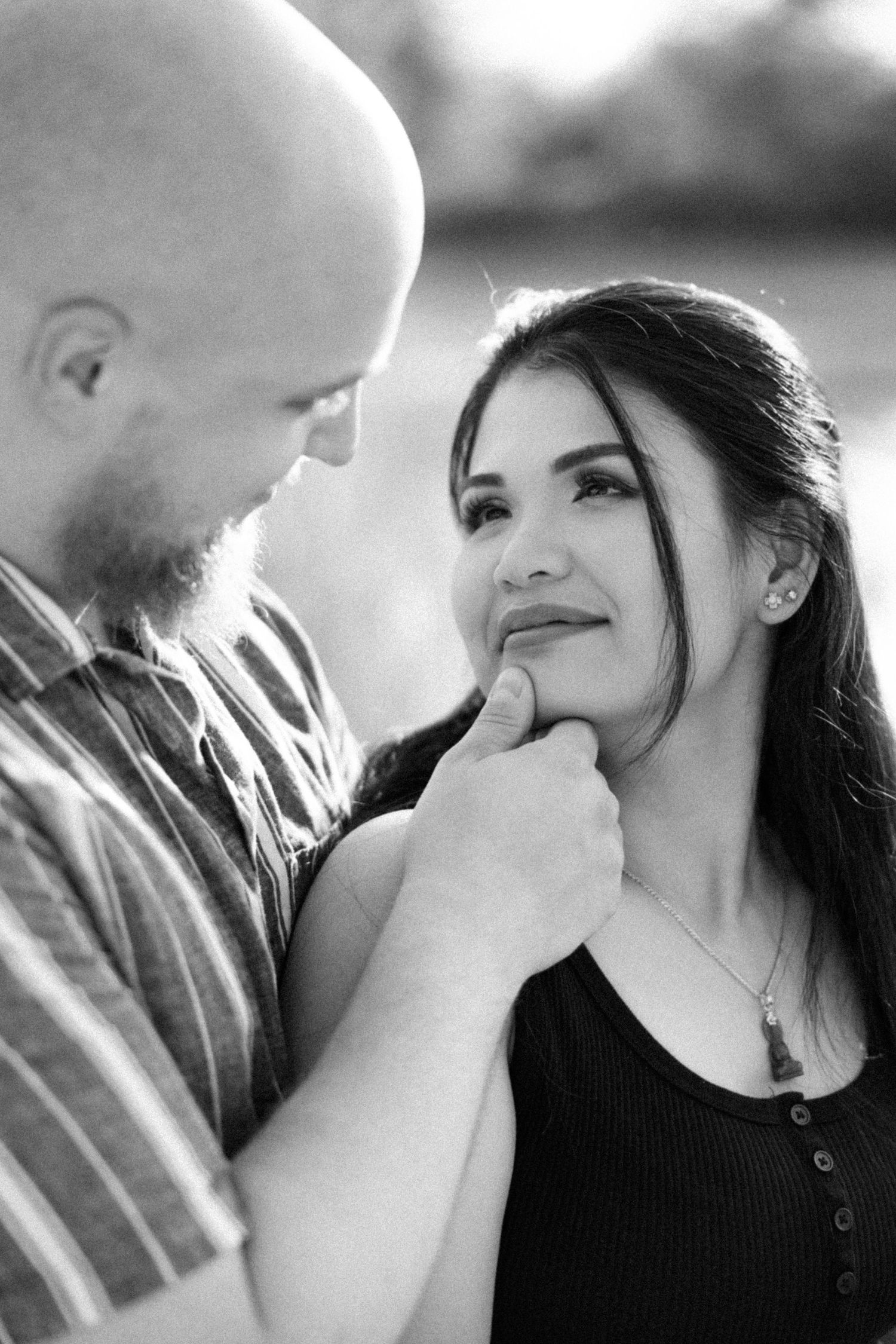 Black and white romantic portrait of a couple sharing an intimate moment outdoors in soft natural lighting.
