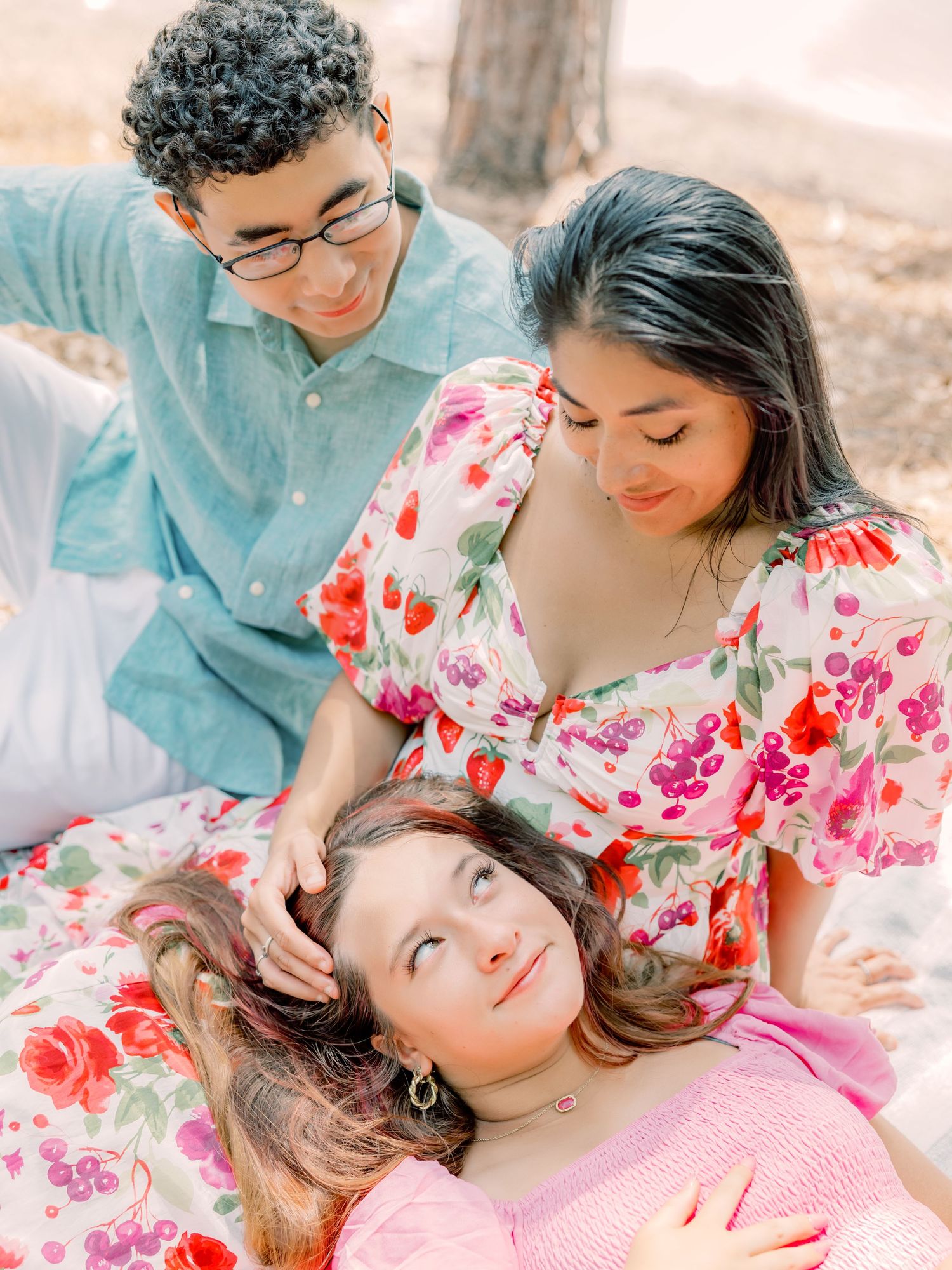 A group shares a tender moment while relaxing together on a blanket outdoors in soft natural lighting.