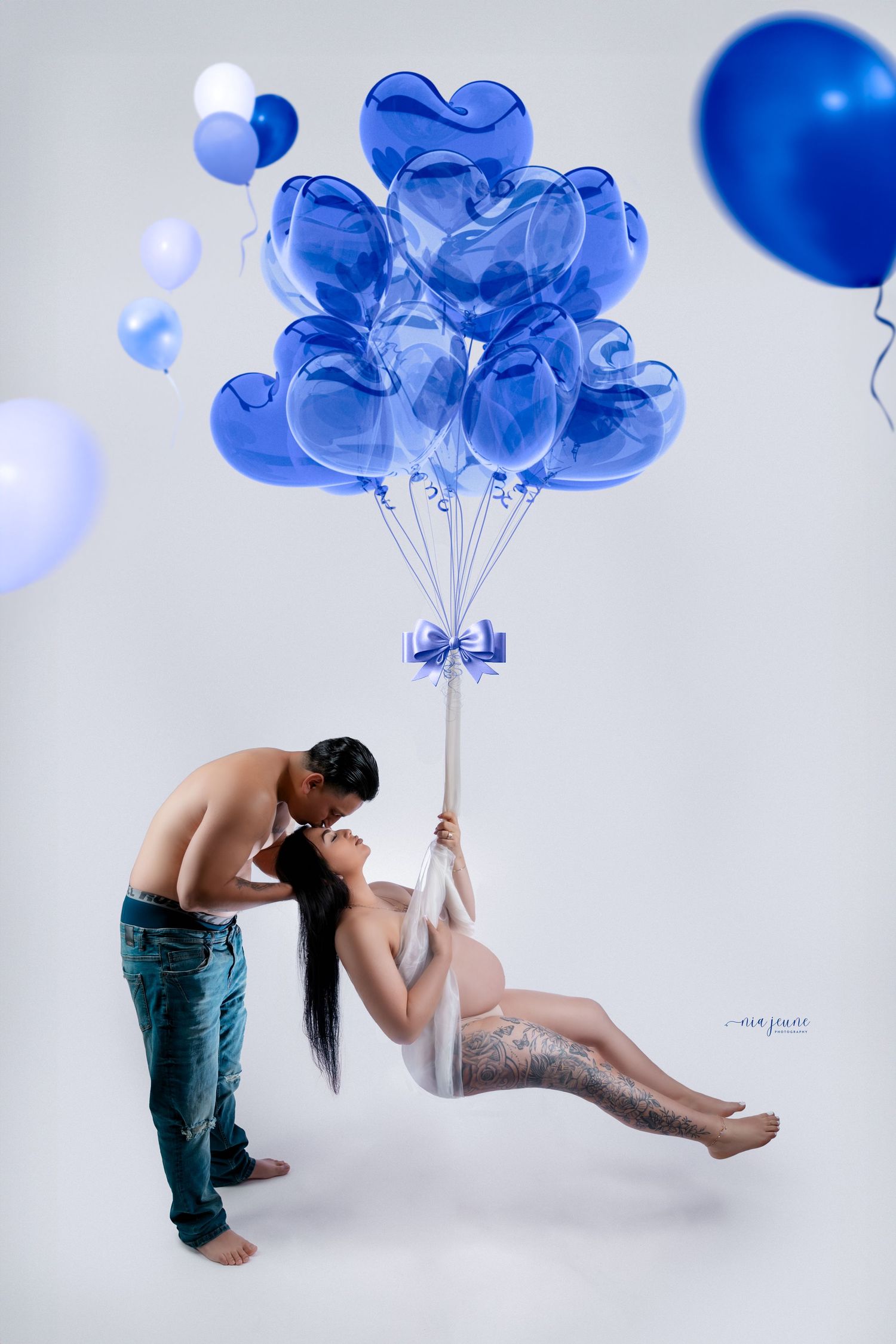 Artistic maternity photoshoot with blue balloons in a white studio setting.