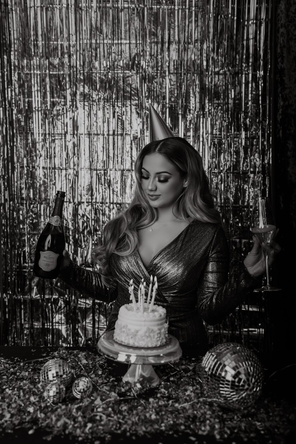 Black and white birthday photo with cake, champagne and metallic backdrop.