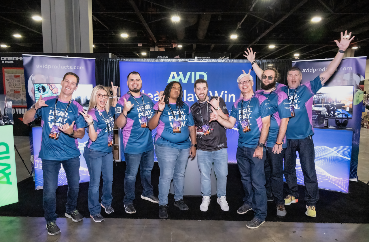 Group of enthusiastic team members in blue shirts celebrating at a tech conference booth.