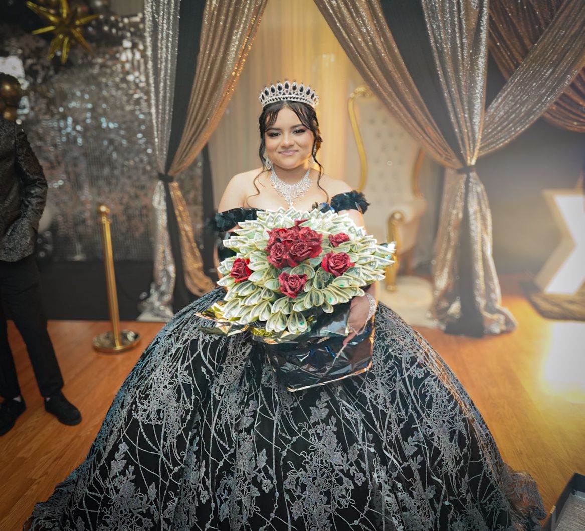 Formal portrait with black ball gown and red bouquet against silver curtain backdrop.