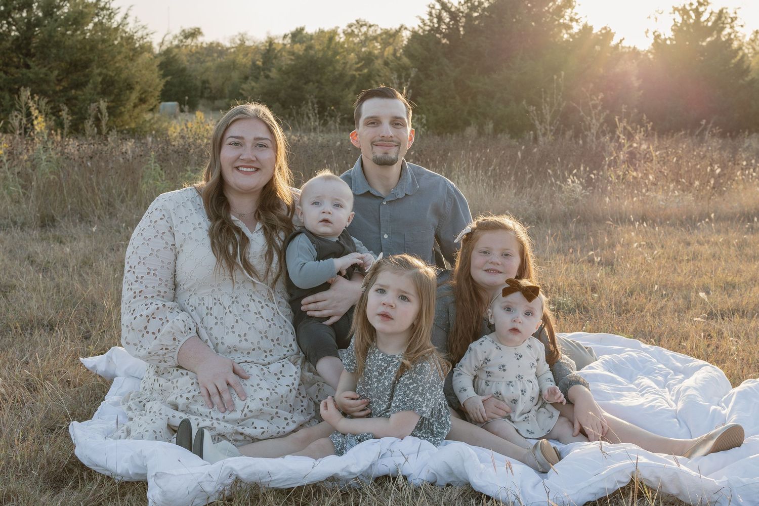 A family portrait at sunset in a rustic field wearing coordinated cream and white outfits.