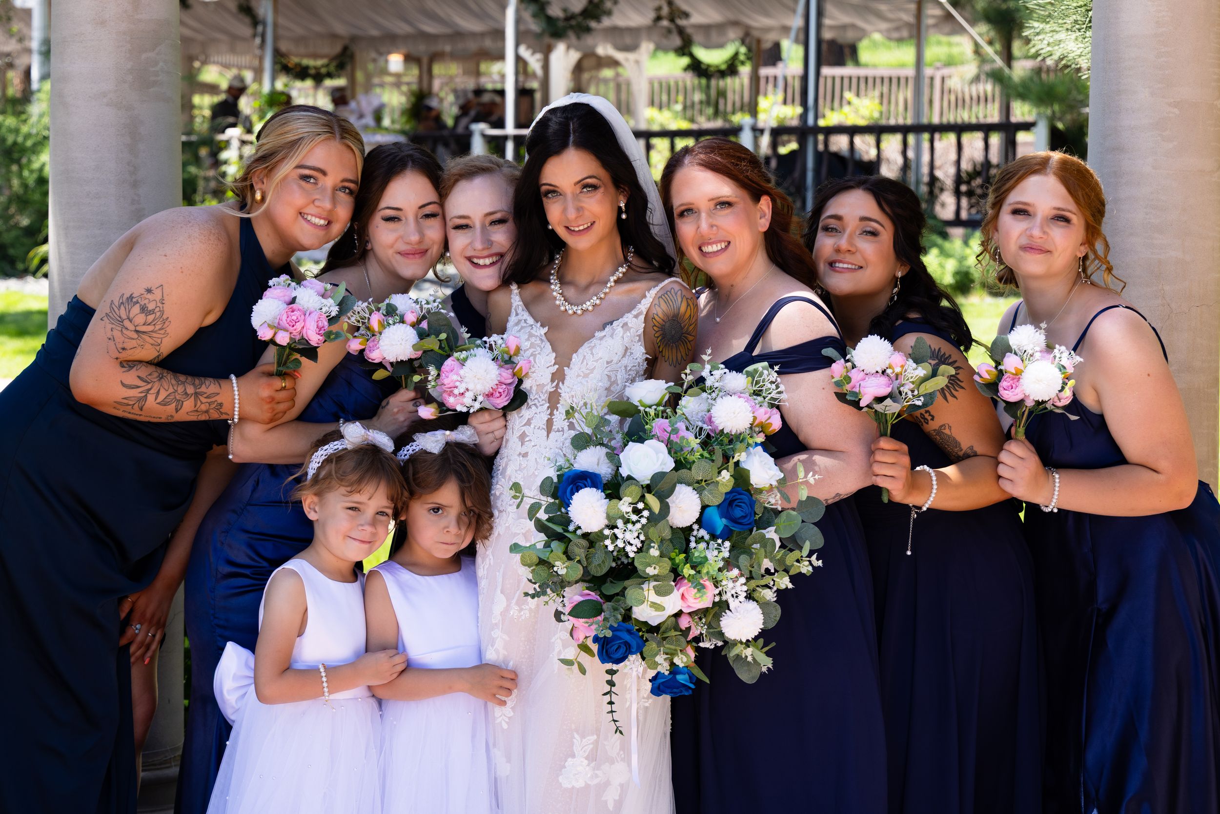 A wedding party wearing navy blue and white poses together for formal photos on a porch with floral bouquets.