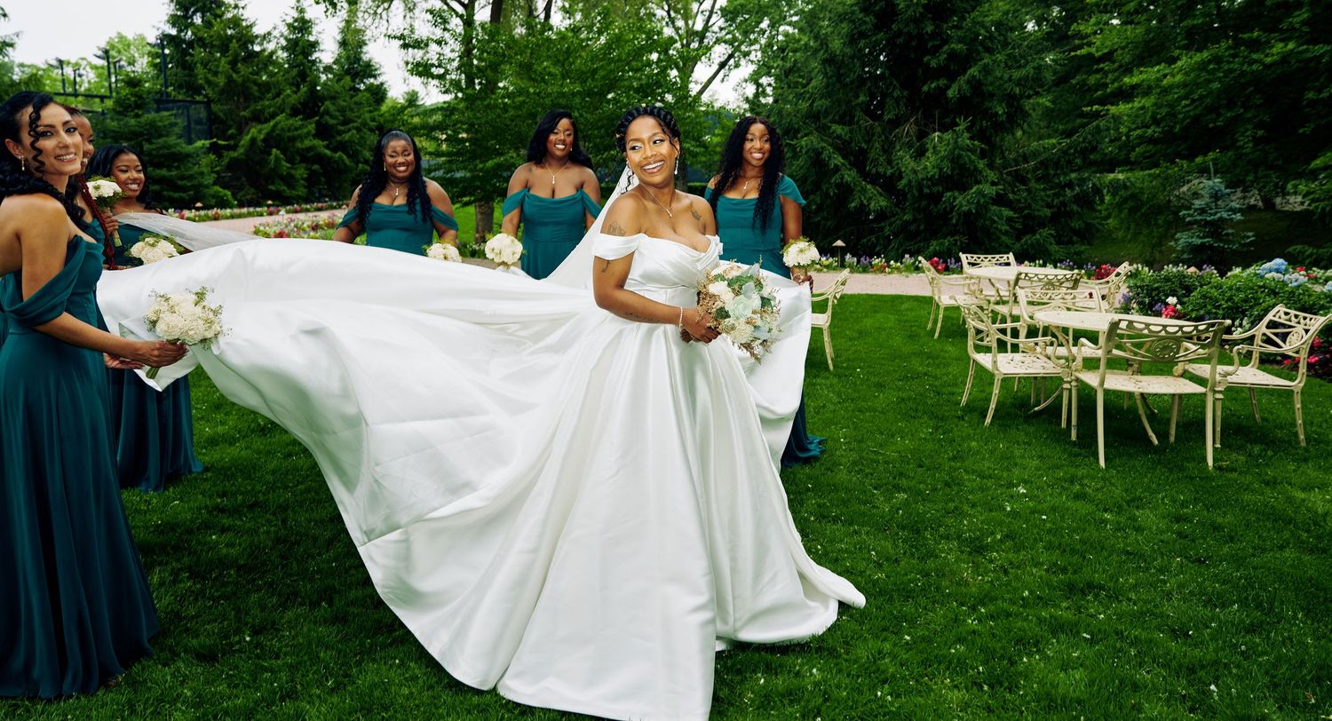 Wedding party on manicured lawn with bride in flowing white gown and bridesmaids in teal dresses.