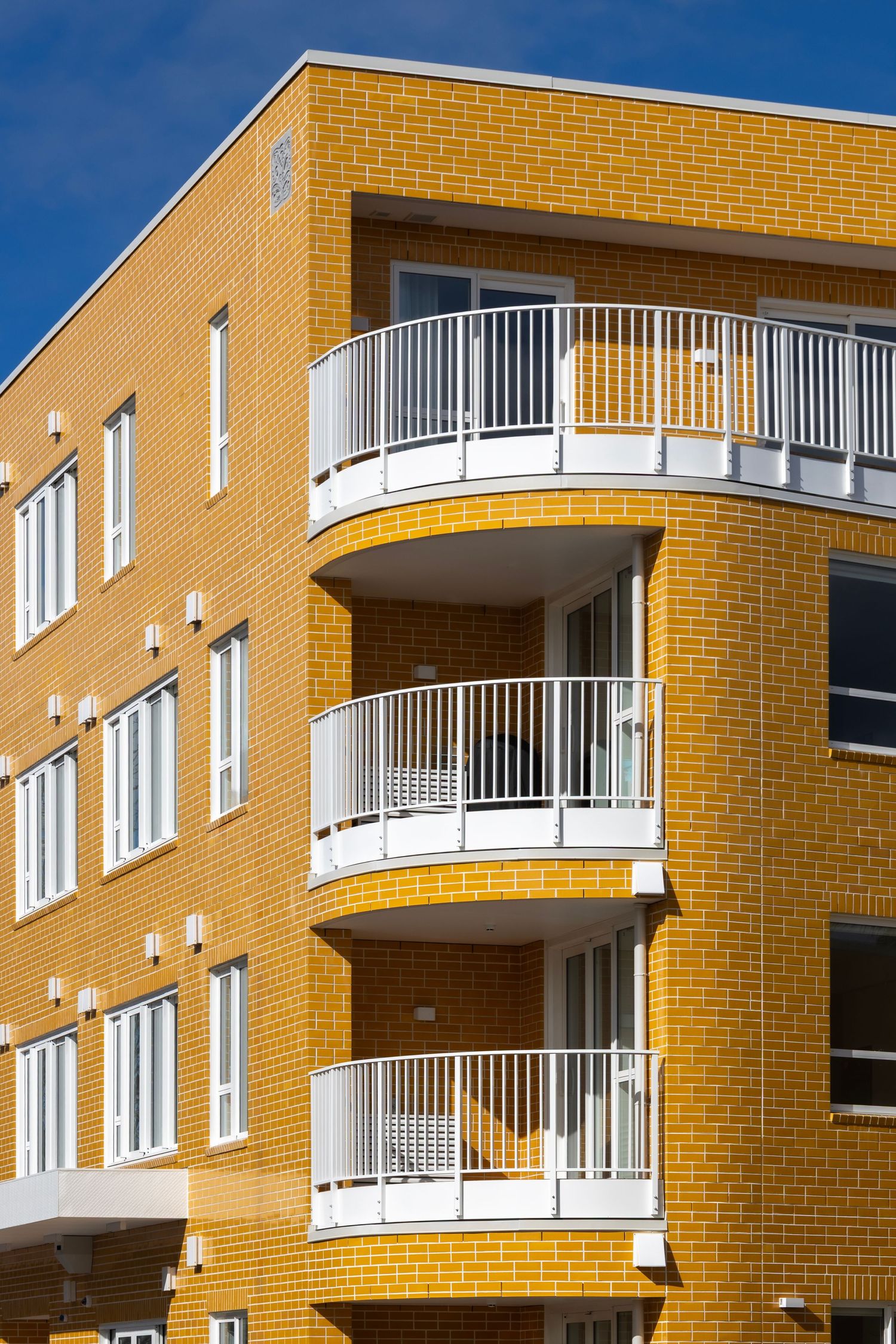 Bright orange brick apartment with curved white balconies catching morning light against blue sky.