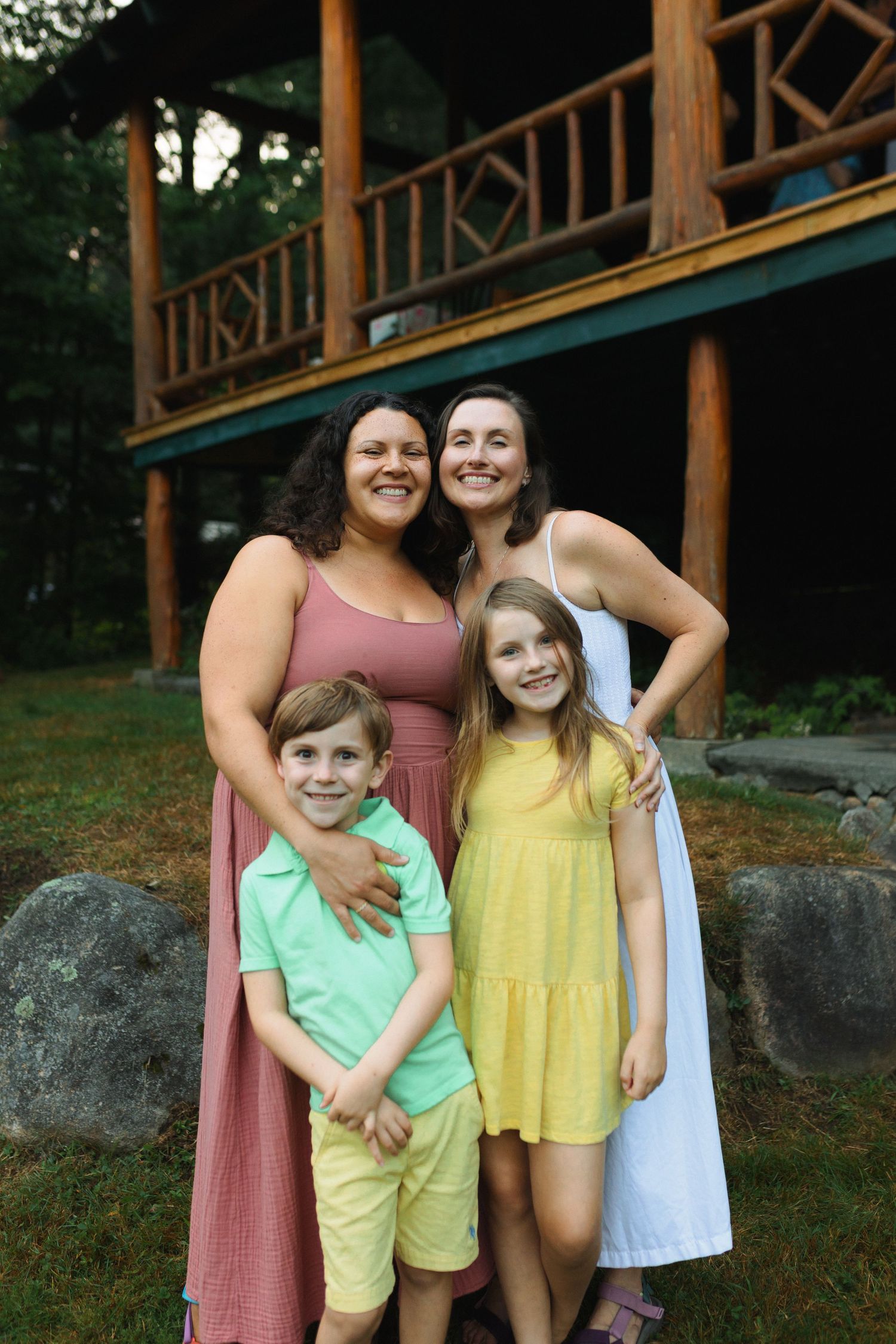 A family poses together on a summer evening in front of a rustic cabin with wooden railings.