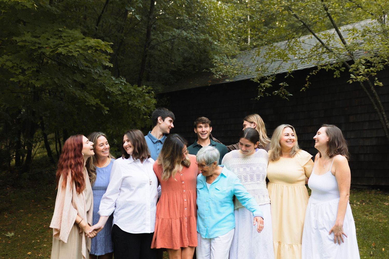 A group of friends in colorful summer outfits standing together and laughing in a wooded outdoor setting.