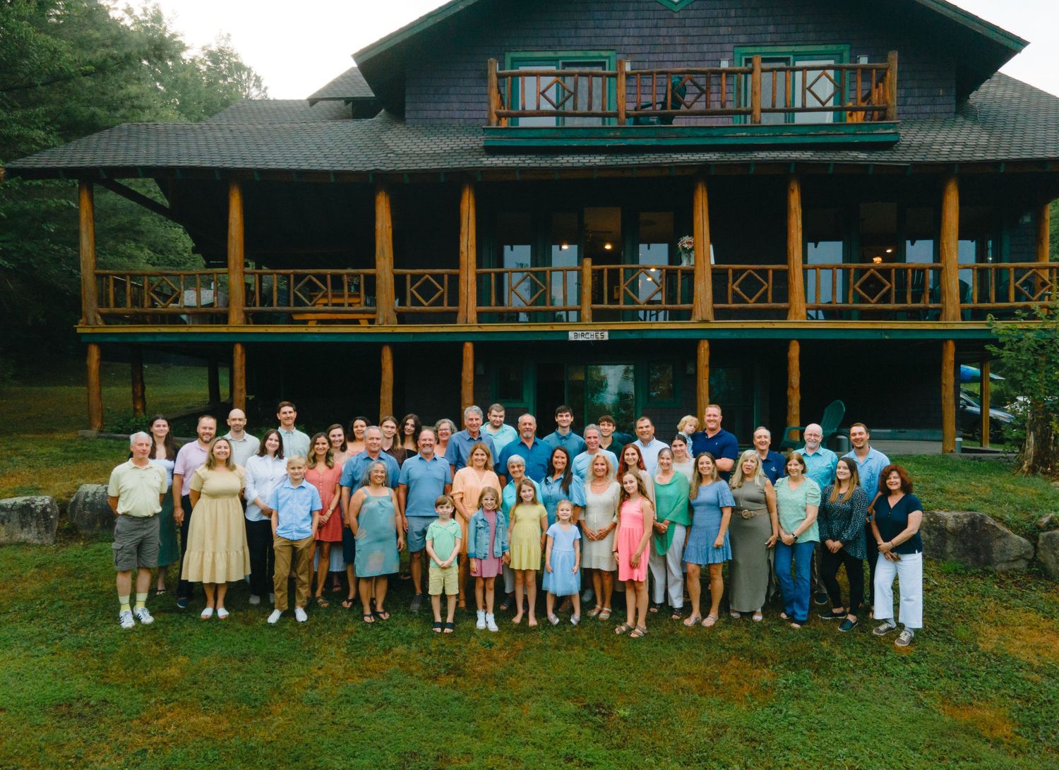 Large group photo of people gathered outside a rustic lodge building with wood trim and balconies.
