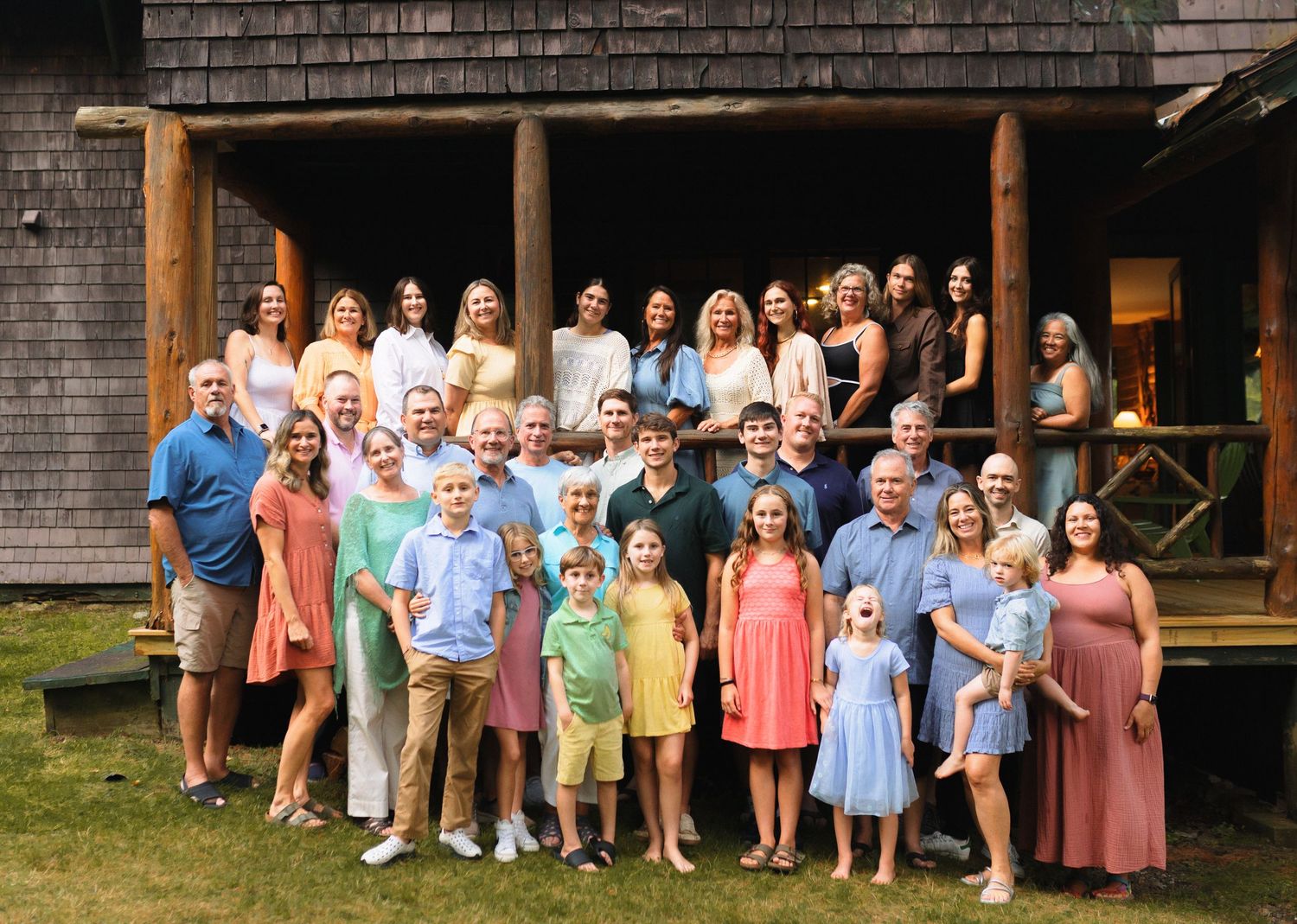 Large family group posing together in front of a rustic wooden cabin during a summer gathering.