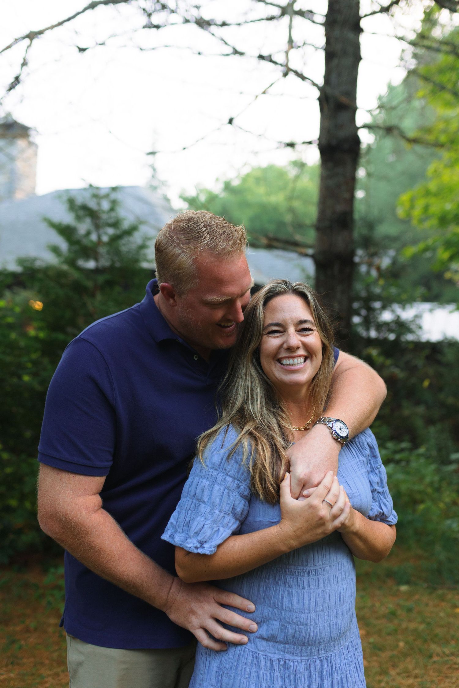 A couple shares a joyful moment together outdoors in a forest setting, embracing and laughing.