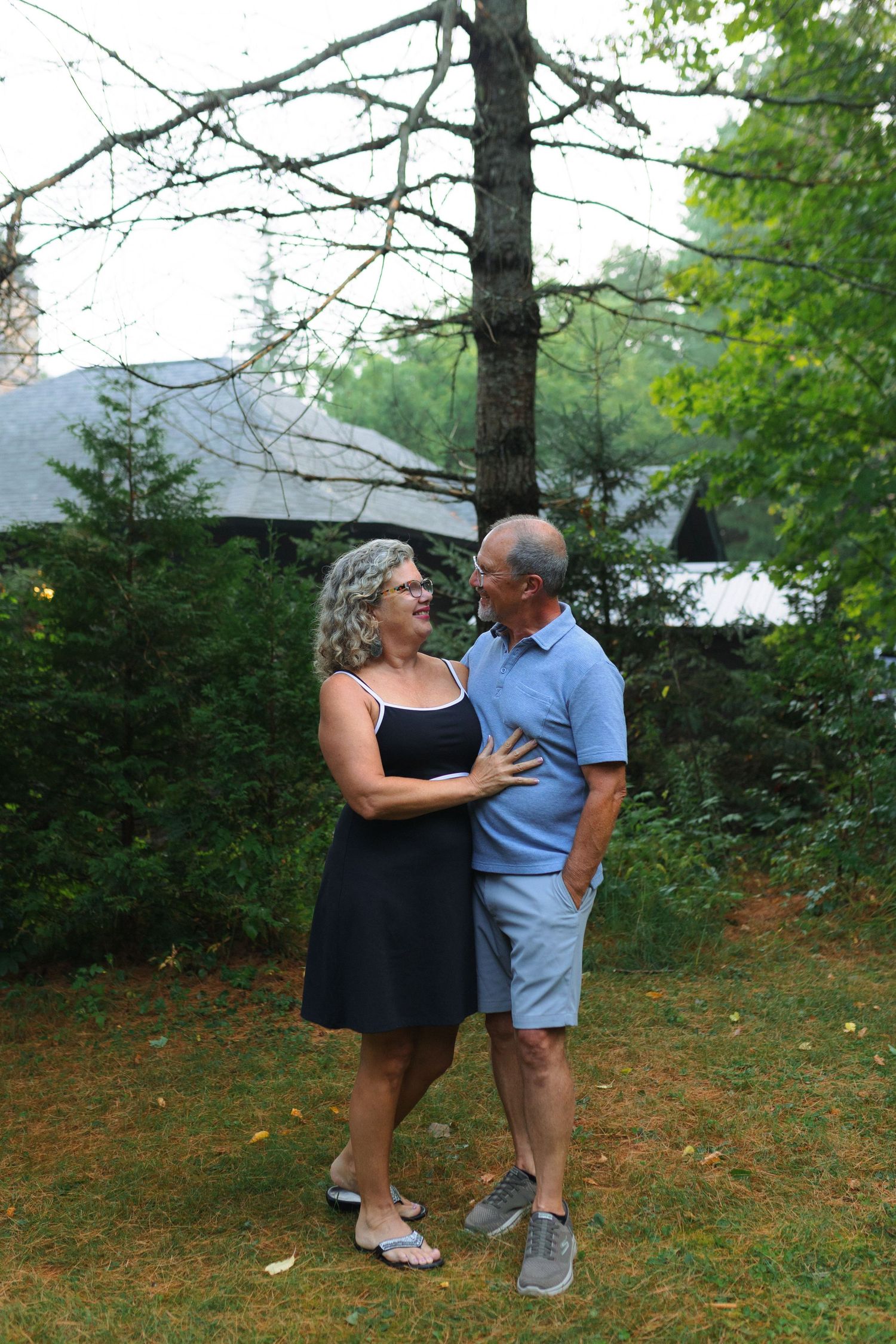 A couple shares a tender moment dancing together on grass near trees beside a lake.