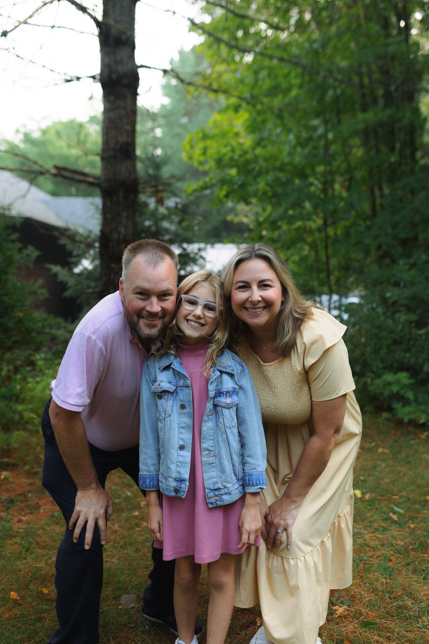 A family poses together outdoors in a wooded setting on a fall day, wearing casual attire.