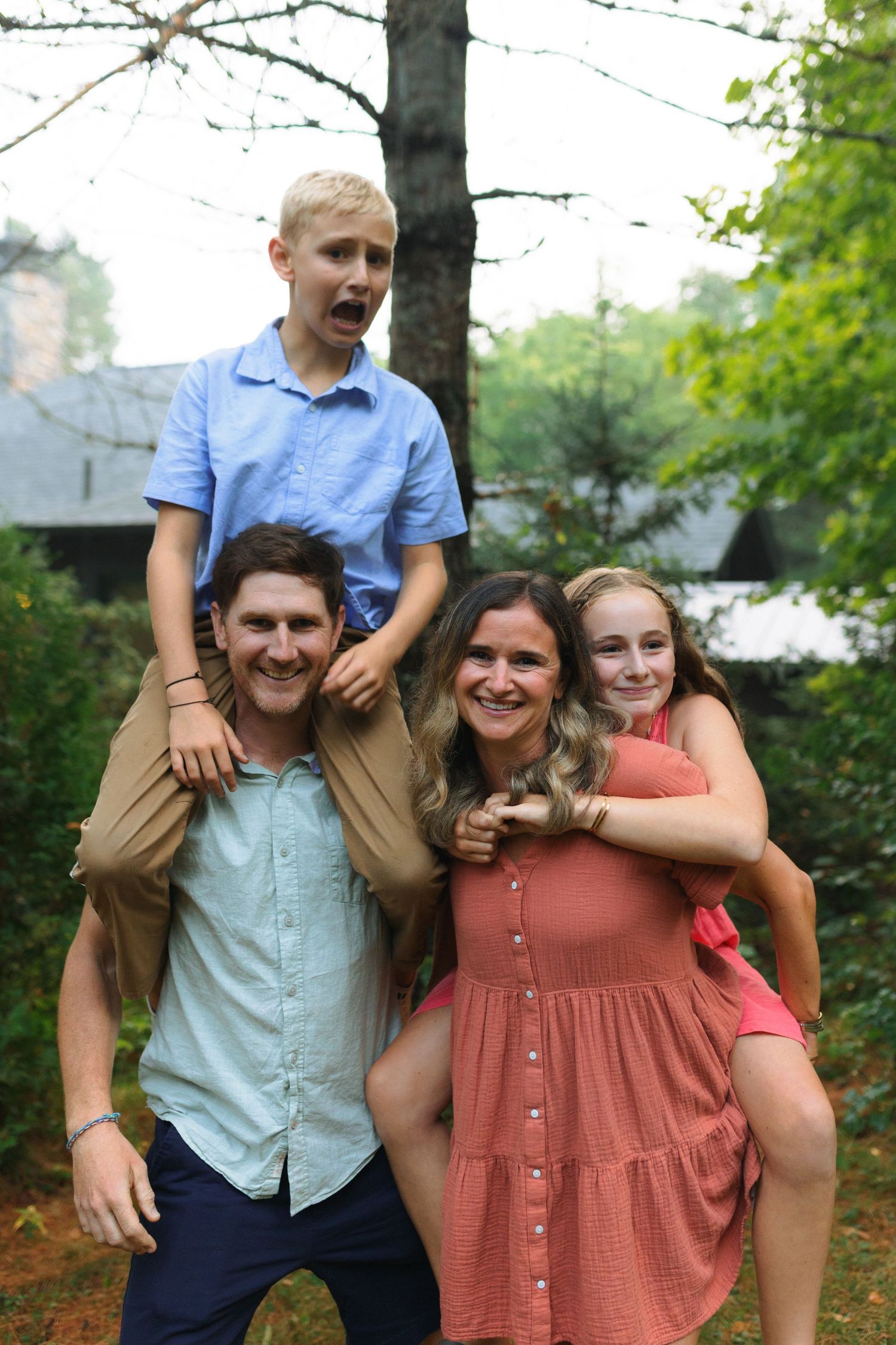 A cheerful group poses together outdoors against a backdrop of green trees on a summer day.
