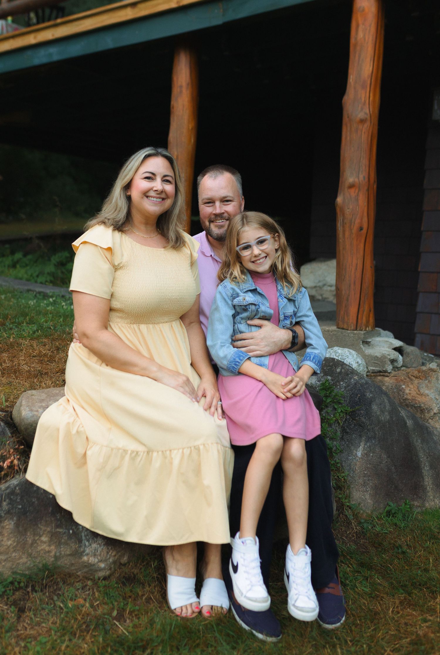 A family sits together on wooden steps outside a rustic cabin surrounded by nature.