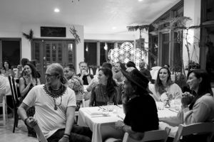 A black and white photo of people gathered around tables at a social event or dinner.