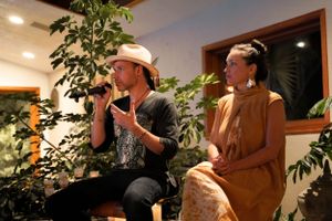 Two performers on stage during an intimate indoor performance with decorative plants.