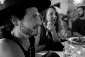 A person wearing a dark hat smiles during what appears to be a dinner gathering.