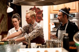 Three chefs collaborating in a warm-lit kitchen during food preparation.