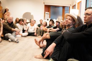A group of people sitting casually on the floor during an indoor gathering.