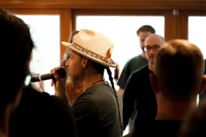 Singer in a cowboy hat performing with a microphone in a casual indoor setting.