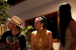 Three people engaged in conversation in a warmly lit indoor setting with natural decor.