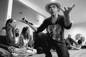 Performer in cowboy hat gesturing expressively while sitting and singing to an audience.