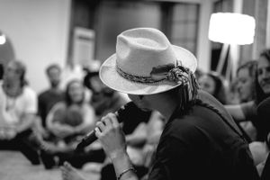 Side profile of a performer with a light-colored hat holding a microphone during an indoor performance.